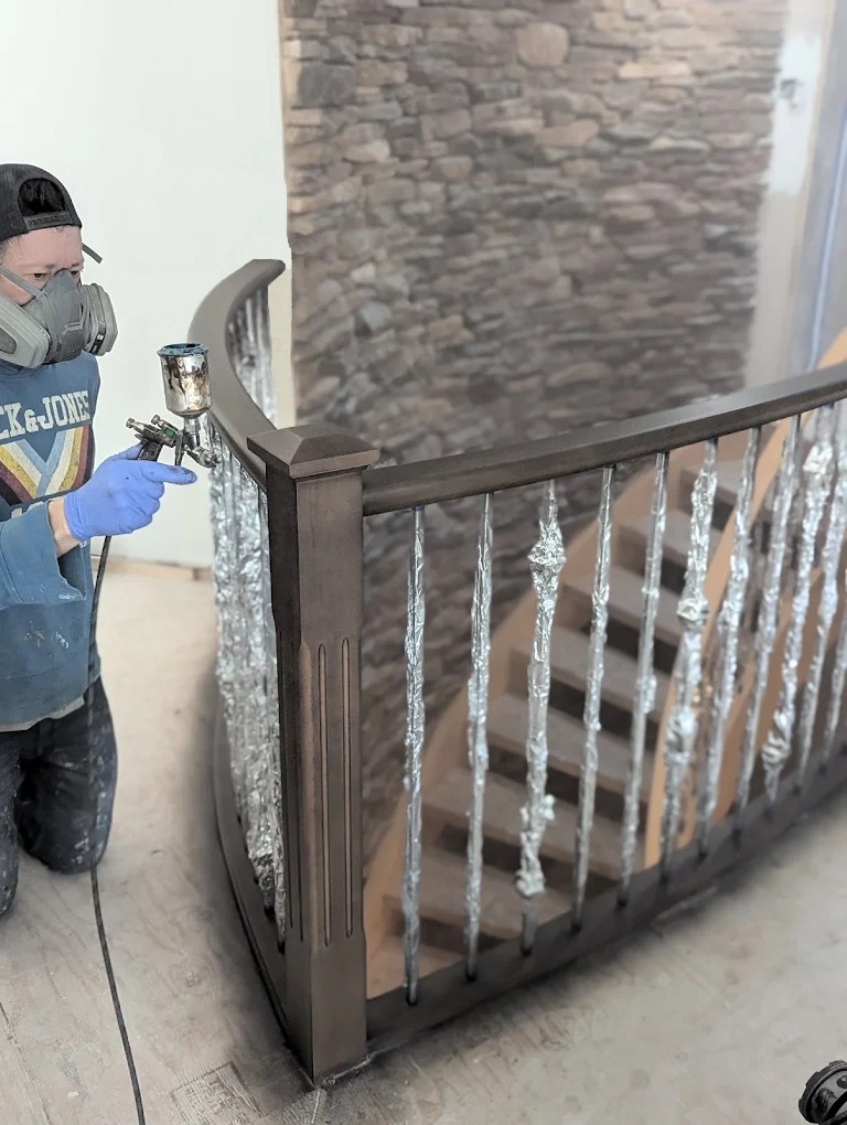 FHG Contracting worker with gas mask on spray painting the rail of a staircase to refinish the wood